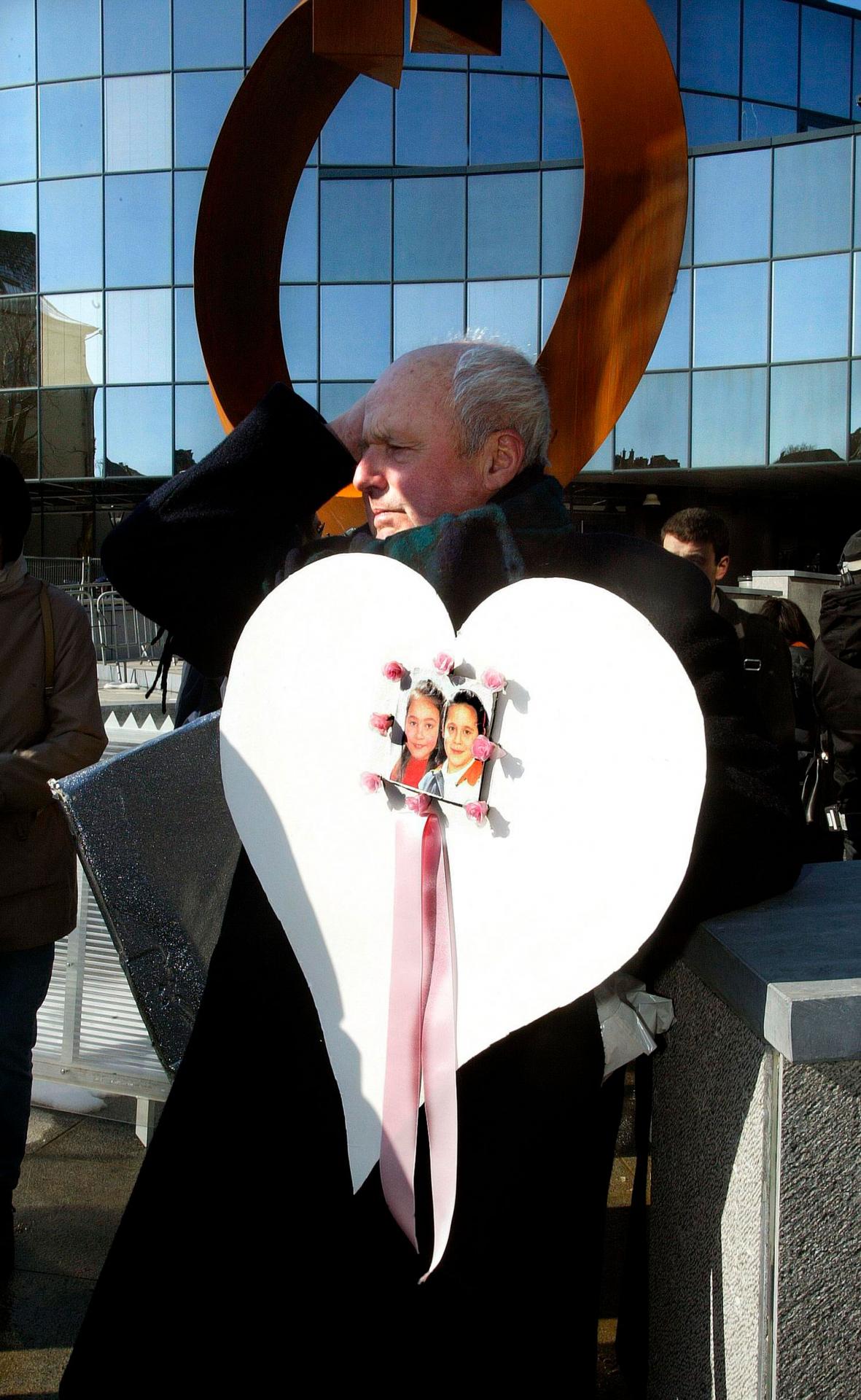 1. marec 2014 Arlon, Belgicko: Muž s fotografiami Julie a Melissy pred budovou súdu počas pojednávania s pedofilným vrahom Marcom Dutrouxom, ktorý znásilnil a týral prinajmenšom šesť dievčat, pričom štyri z nich zavraždil.