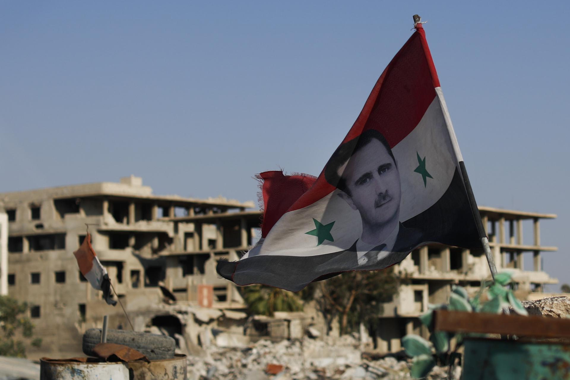 Sýrska vlajka s portrétom prezidenta Baššára al-Asada na vojenskom stanovišti. Režim sa snaží vyvolať u ľudí pocit, že prezident Asad s podporou Ruska a Iránu porazil sýrsku opozíciu.