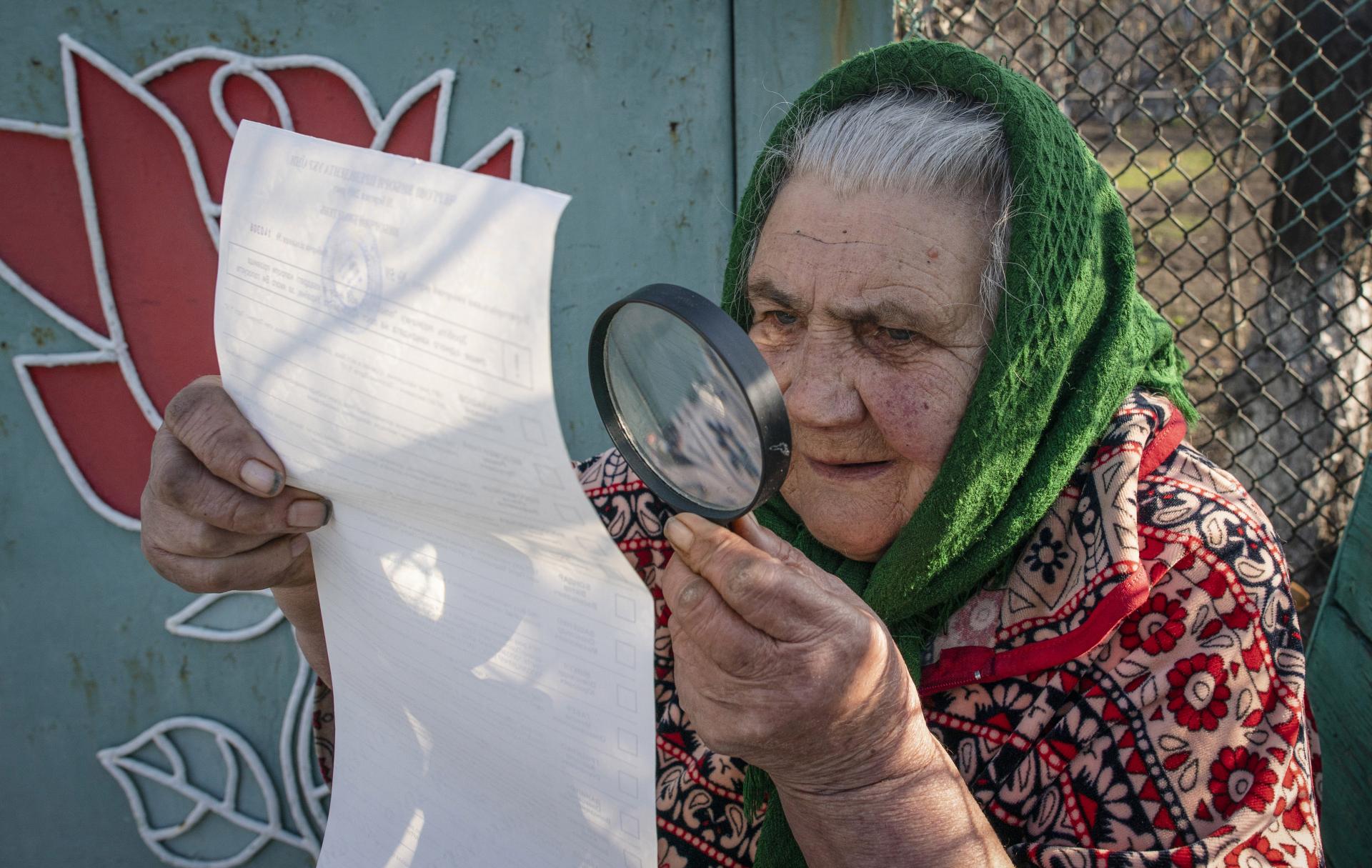 Staršia volička z obce Marjinka na východe Ukrajiny, neďaleko separatistami okupovaného Donecka, si s lupou prezerá zoznam kandidátov na prezidenta.